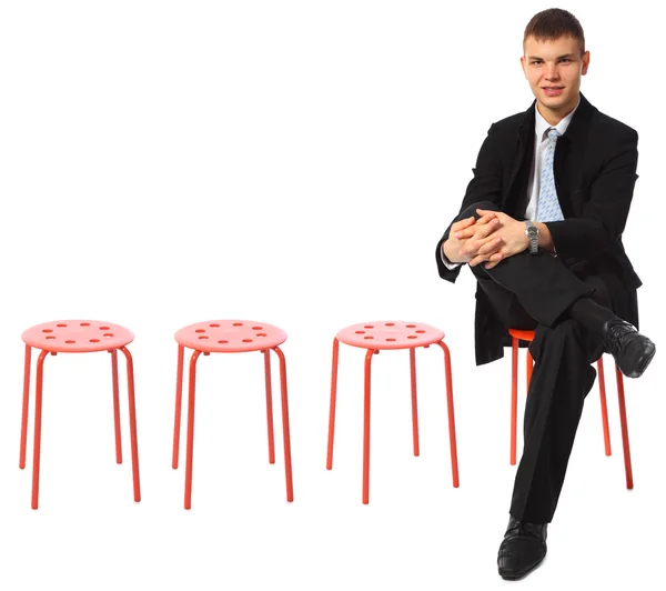 Young businessman sits on red stool leg on leg — Stock Photo, Image