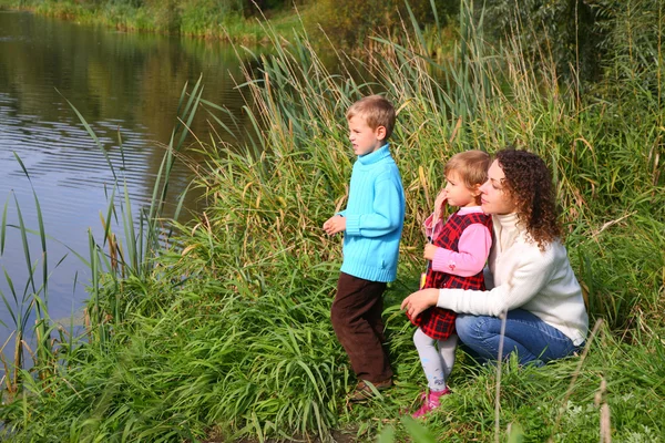 Mutter mit Kindern sitzt am Ufer des Teiches — Stockfoto