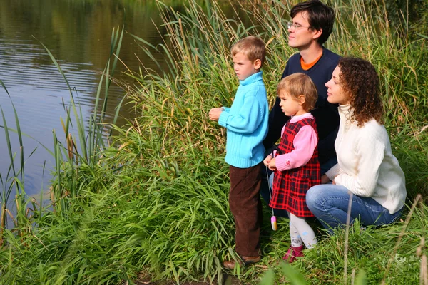 Родители с детьми сидят на берегу пруда — стоковое фото