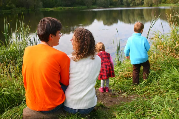 Eltern mit Kindern sitzen am Ufer des Teiches, Rückansicht — Stockfoto