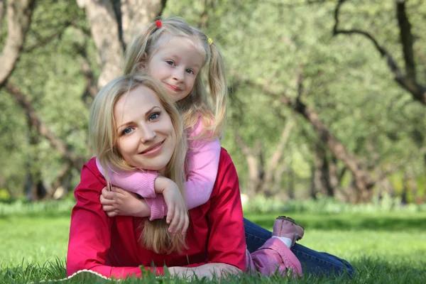 Daughter embraces behind mother lying on grass in park — Stock Photo, Image
