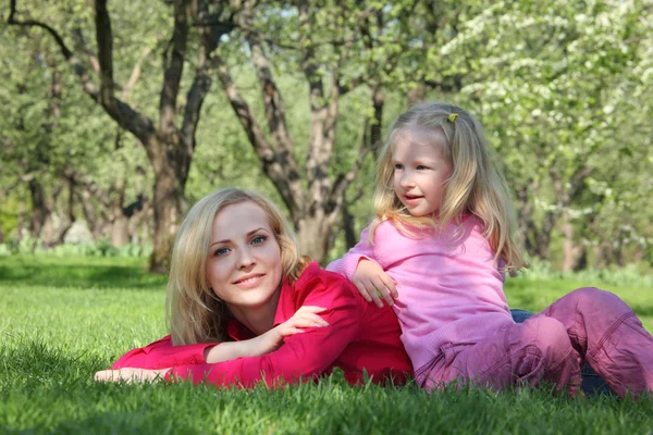 Filha tem cotovelos inclinados na mãe deitada na grama no parque — Fotografia de Stock