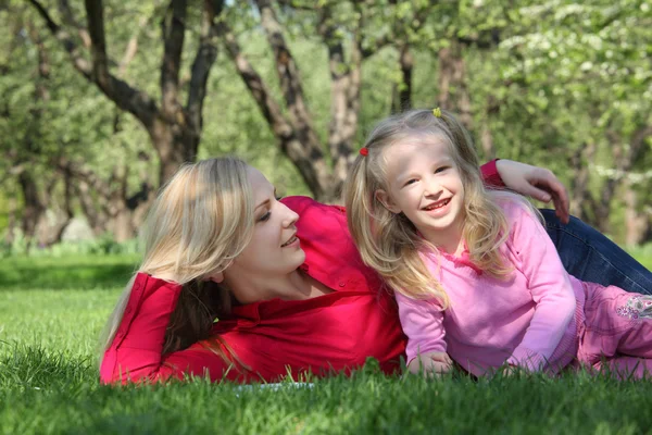 Мать обнимает дочь лежащую на траве в парке — стоковое фото