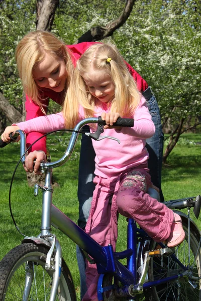 Матері дізнається дочка їхати на велосипеді в весняний сад — стокове фото