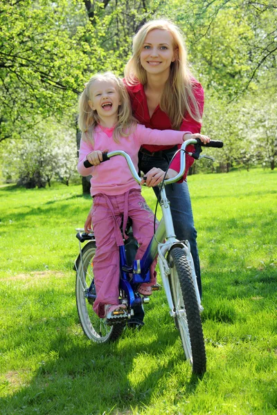 Smějící se dívka na kole s matkou v jarní zahradě — Stock fotografie