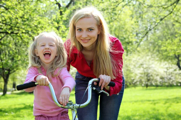Смеющаяся девушка на велосипеде с матерью в весеннем саду — стоковое фото