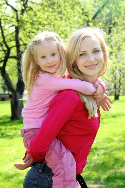 Tochter sitzt auf Rücken der Mutter im Frühlingspark — Stockfoto