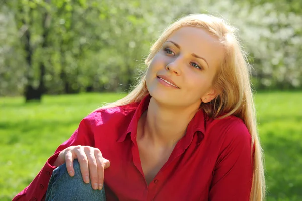 Krásná blondýna sedí na trávě v parku na jaře — Stock fotografie