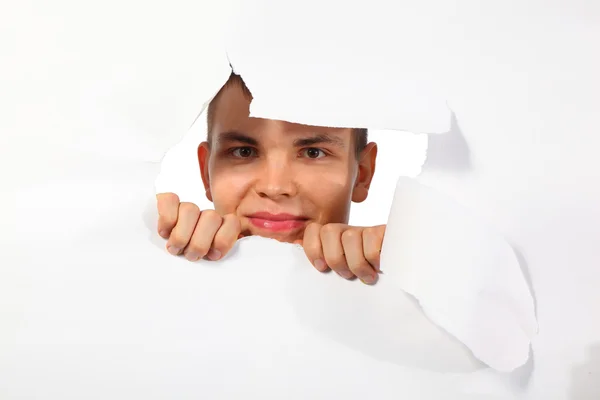 Молодой человек, выглядывающий в дыру в бумаге — стоковое фото