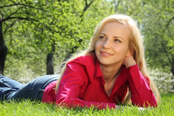 Beautiful blonde lies on grass in park in spring — Stock Photo, Image