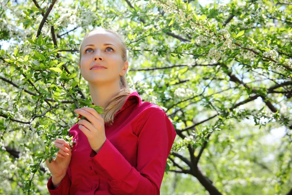 Beautiful blonde looks upward in blossoming garden in spring — Stock Photo, Image