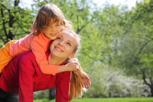 Daughter lies at mother on back in spring park — Stock Photo, Image