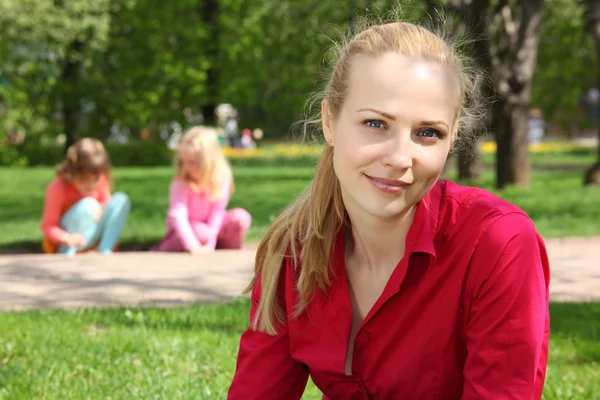 Piękna blondynka w parku z bawiące się dzieci na tle — Zdjęcie stockowe