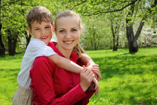 Son omfamnar bakom mor i parken under våren — Stockfoto