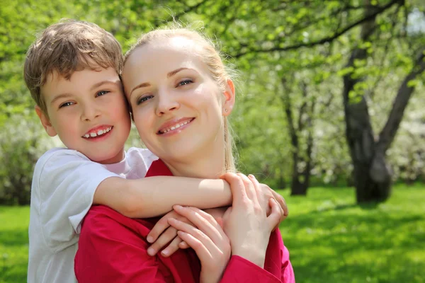 Son embraces behind mother for neck in park in spring — Stock Photo, Image