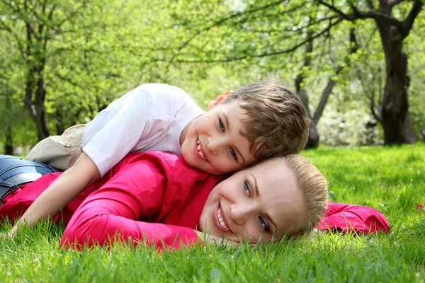 Hijo se acuesta en la espalda de la madre acostada en la hierba en el parque en primavera —  Fotos de Stock