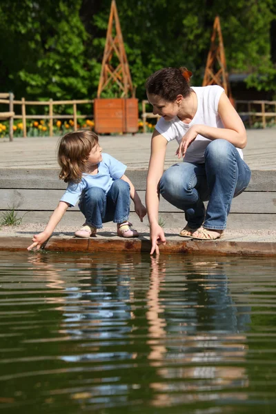 Мати з дочкою в парку біля басейну торкаються води — стокове фото