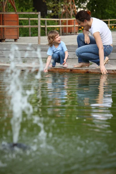 Mother with daughter in park at pool with fountain touch water — Stock Photo, Image
