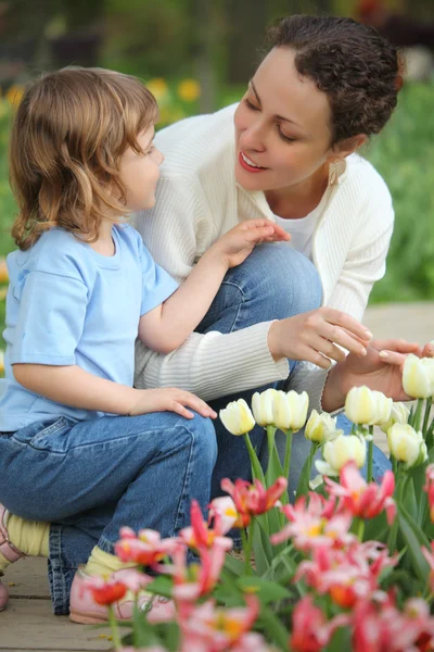 La bambina insieme con madre si siede a letto con tulipani — Foto Stock