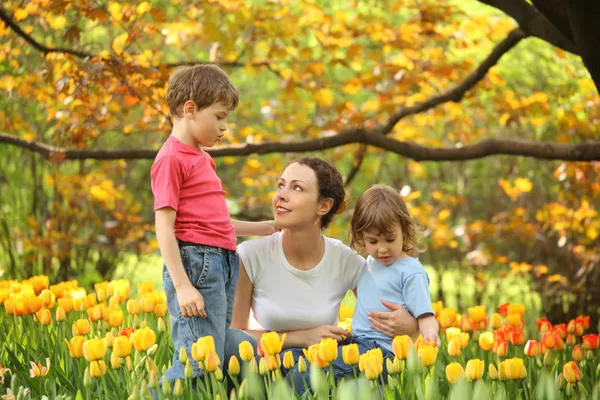 Moeder met kinderen in de tuin in het voorjaar onder bloeiende tulpen — Stockfoto