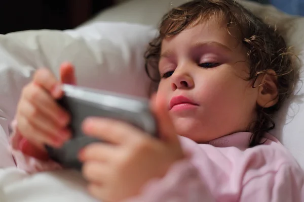 Petite fille au lit avec ordinateur hendheld — Photo