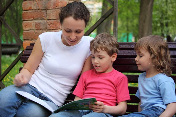 Mãe com crianças sentar no banco e ler livro — Fotografia de Stock