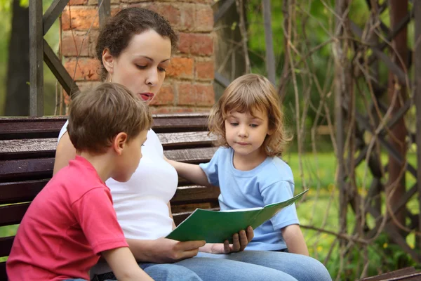 Μητέρα με τα παιδιά κάθονται στον πάγκο και διαβάσει το βιβλίο — Φωτογραφία Αρχείου