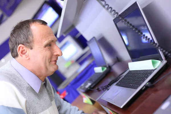 Elderly man in shop looks at laptop — Stock Photo, Image