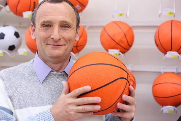 Äldre man i butik med basket boll i händerna — Stockfoto
