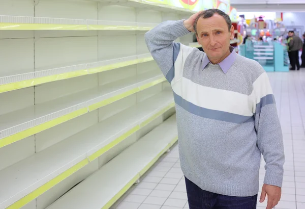 Anciano en estantes vacíos en tienda arañazos en nuca — Foto de Stock