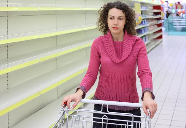 Mujer joven con carro en tienda con estantes vacíos —  Fotos de Stock