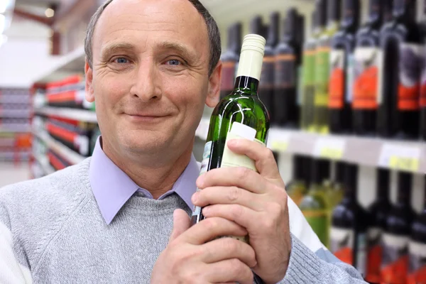 Gelukkig bejaarde man in winkel met fles wijn in handen — Stockfoto