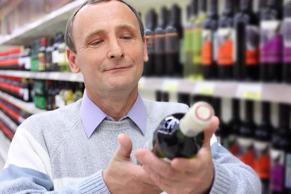 Gelukkig bejaarde man in winkel kijkt op fles wijn in handen — Stockfoto