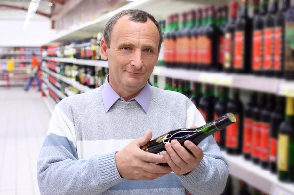 Oudere man in winkel met fles wijn in handen — Stockfoto