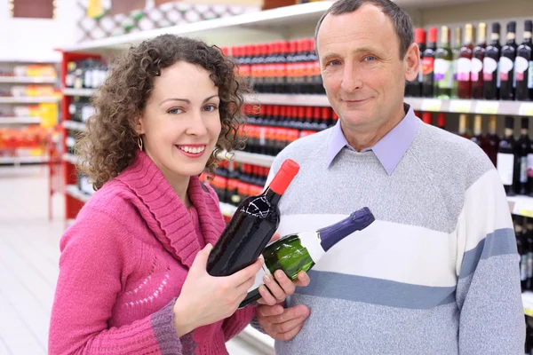 Glad tjej och äldre man i butik med vinflaskor i händer — Stockfoto