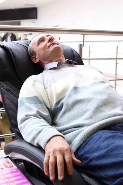 Äldre man ligger i massage fåtölj — Stockfoto