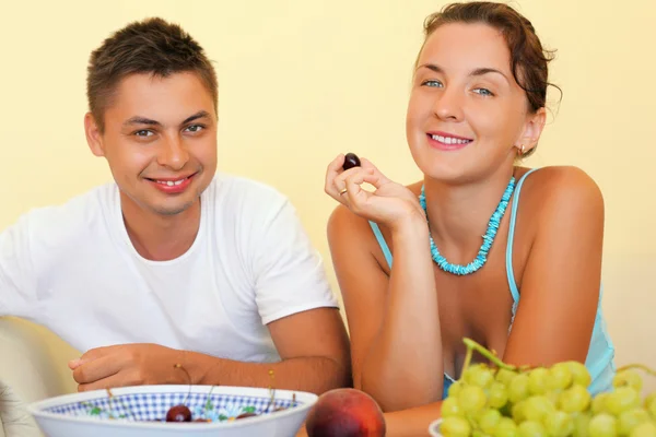 Sonriente hombre y mujer joven comer fruta en habitación acogedora —  Fotos de Stock
