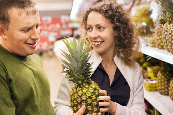 Lachende jonge man en vrouw kopen ananas in supermarkt — Stockfoto