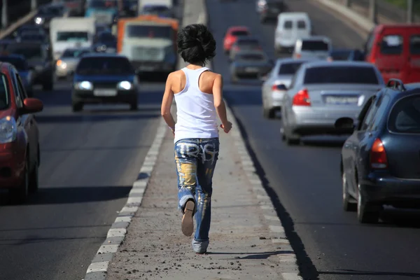 Chica corre en medio de la autopista en la ciudad, vista desde atrás — Foto de Stock