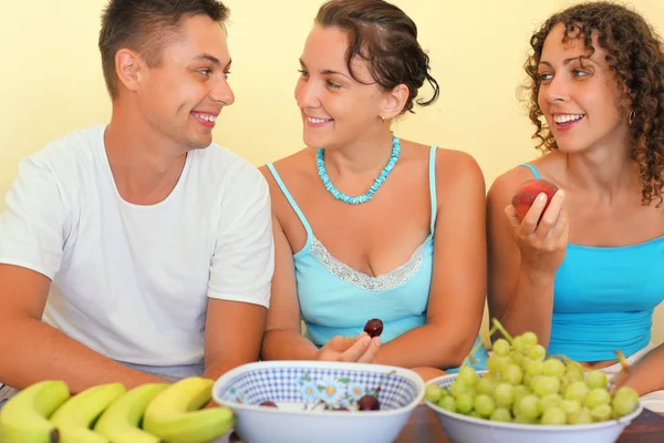 Улыбающийся мужчина и две молодые женщины едят фрукты в уютной комнате — стоковое фото
