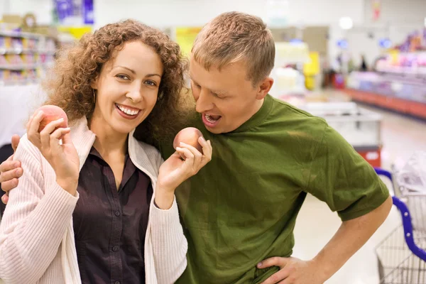 Sonriente joven hombre y mujer comprar melocotones en el supermercado —  Fotos de Stock