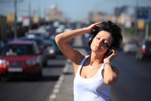 Girl listens music in ear-phones on highway middle — Stock Photo, Image
