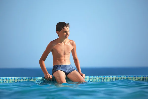 Tiener jongen wets meter water in het zwembad tegen zee — Stockfoto