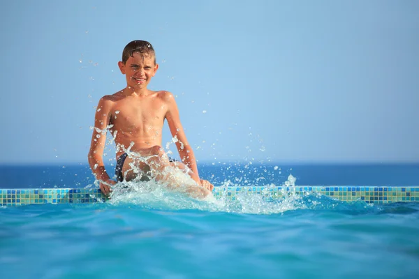 Tiener jongen spatten meter water in het zwembad tegen zee — Stockfoto