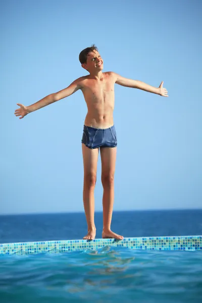 Tonåring pojke står nära pool mot havet, växter händer i par — Stockfoto