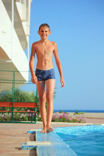 Adolescente ragazzo andando vicino piscina contro mare — Foto Stock