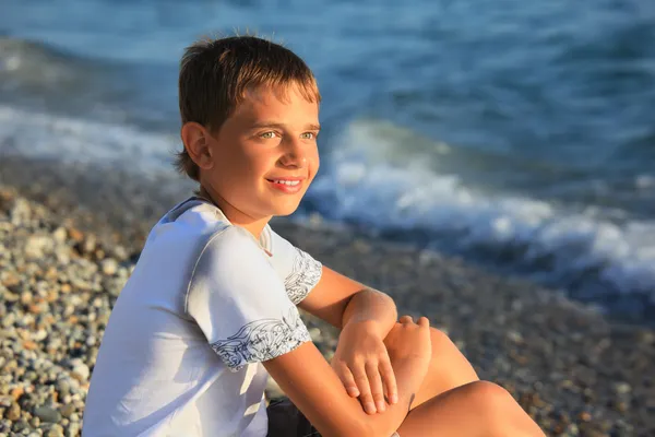 Assis adolescent garçon sur pierre bord de mer — Photo