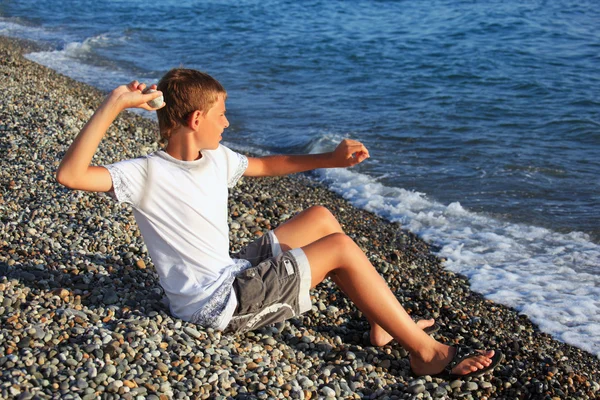 Seduta ragazzo lancia pietra in mare — Foto Stock