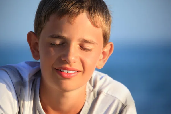 Genç çocuk denize karşı gülümsüyor, gözler kapalı. — Stok fotoğraf