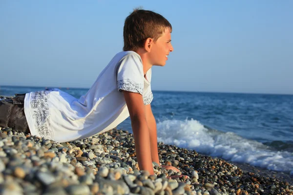 Teenager boy lying on stones on seacoast — Stock Photo, Image